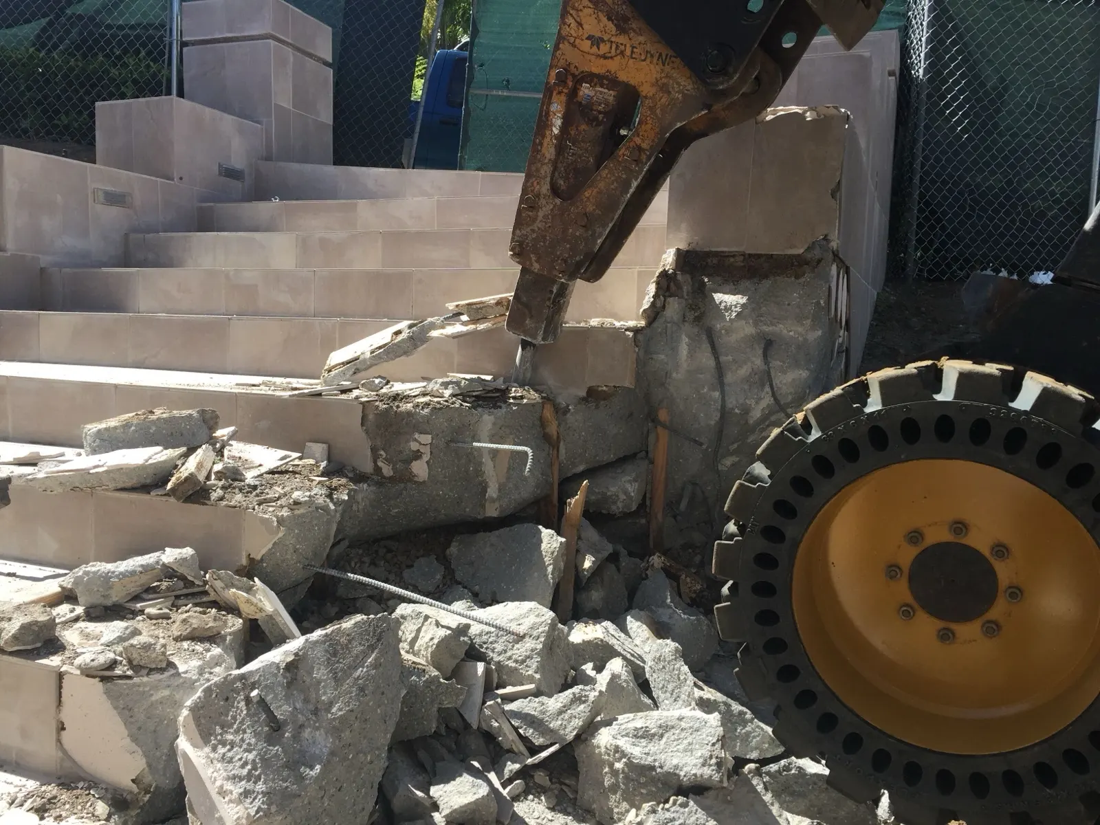 Hydraulic breaker on a skid steer taking apart concrete steps and block walls