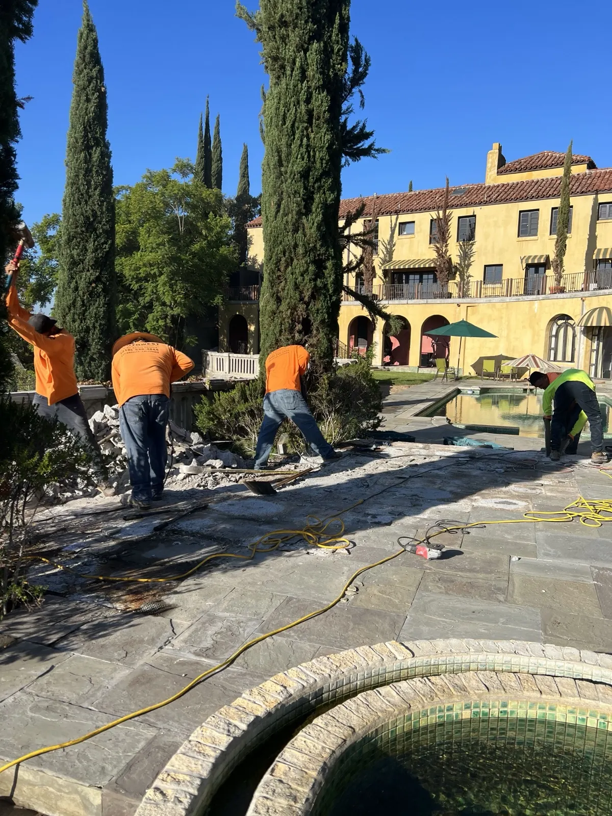 Crew pulling up flagstone hardscape beside the pool at a large property