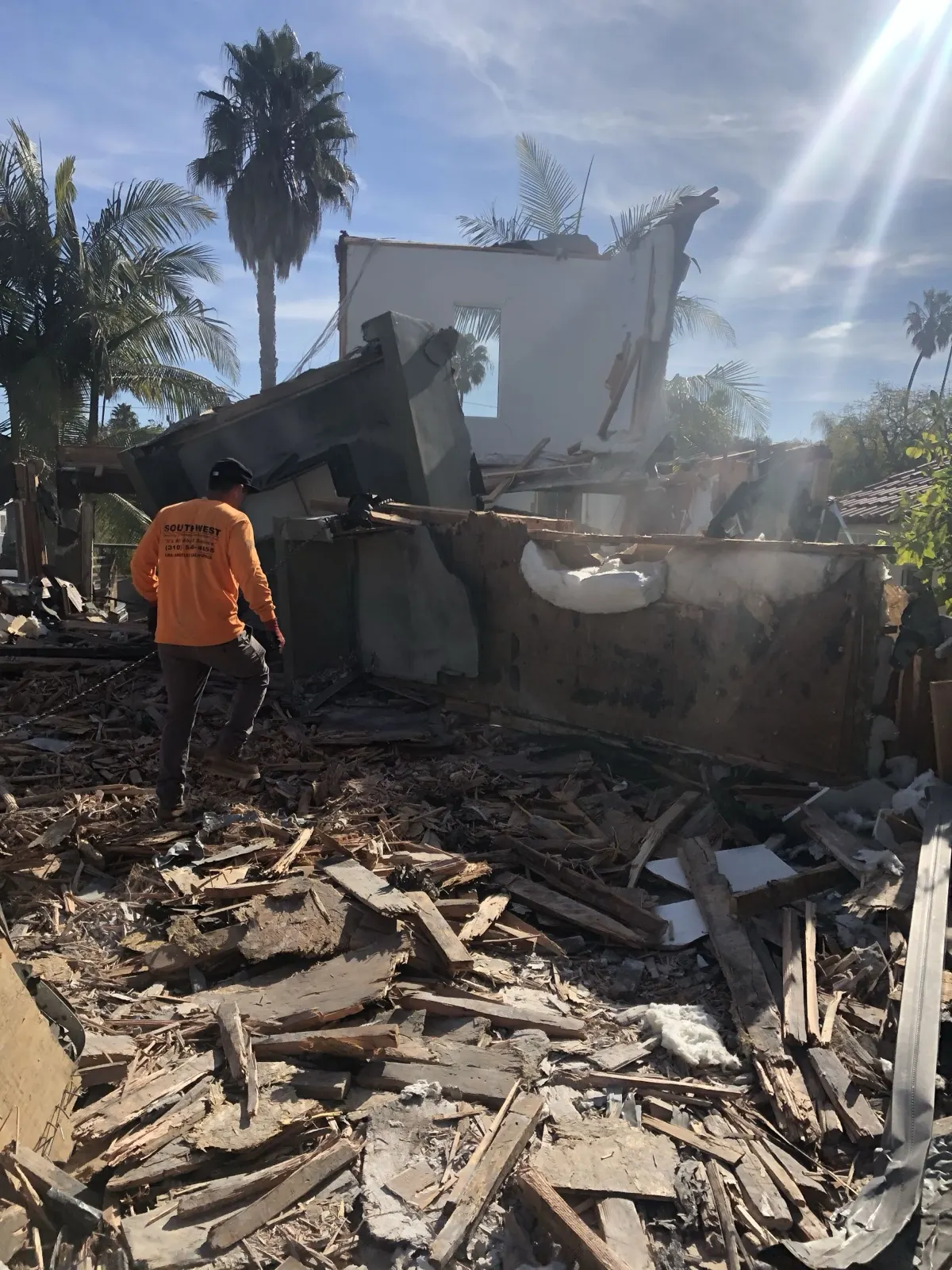 Crew member walking a house demolition site with the structure down and debris spread