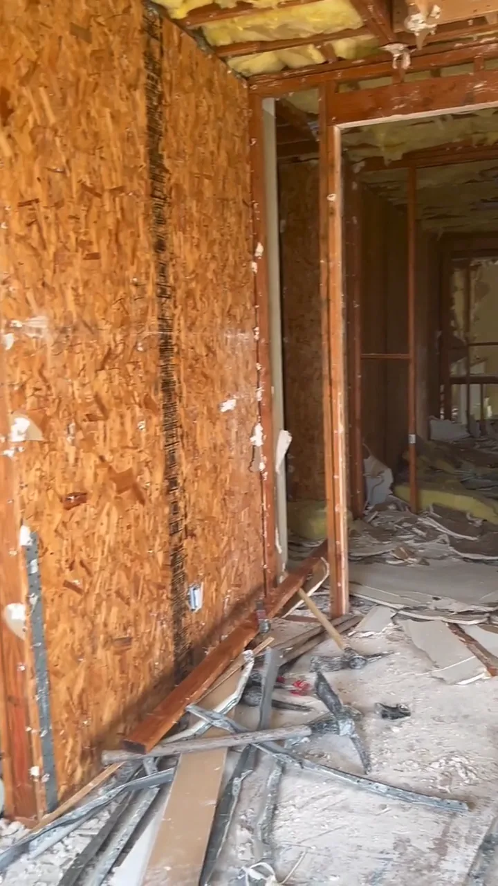 Drywall torn out down to the wall sheathing, with demolition debris across the floor